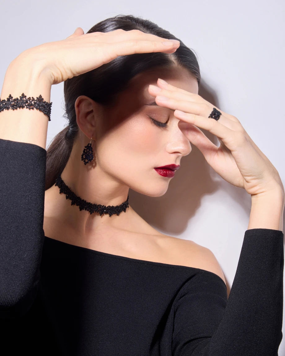 Black AIRA bracelet on wrist with lace pattern, paired with matching choker and earrings, worn by model.