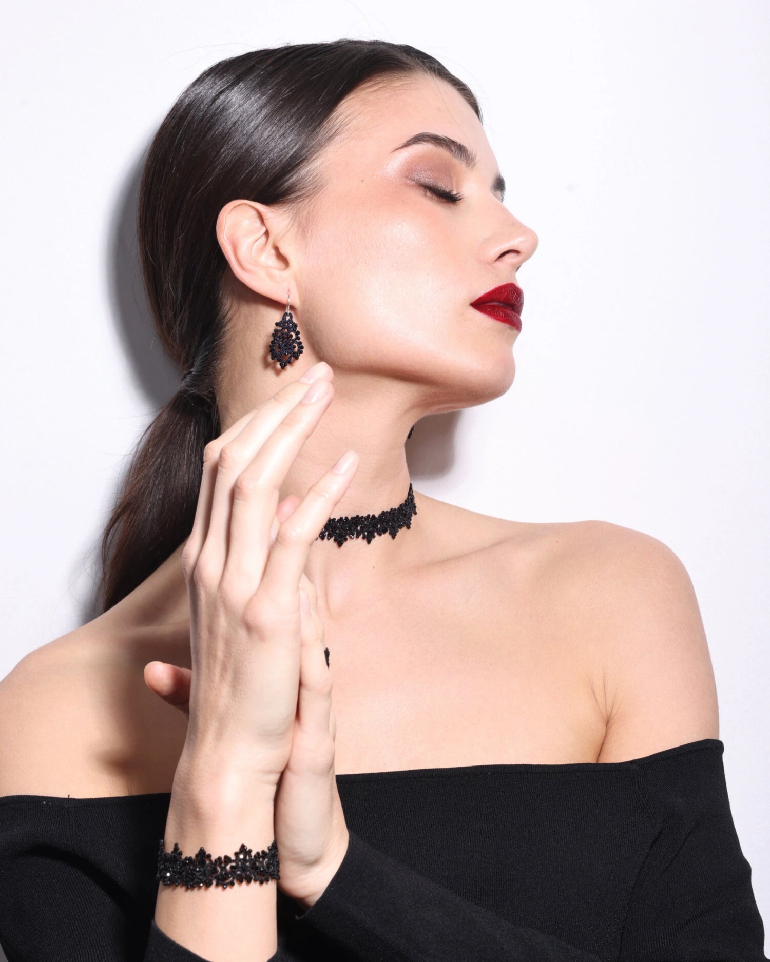 Black AIRA choker with intricate lace detail, side view, worn with matching bracelet and earrings, elegant style.