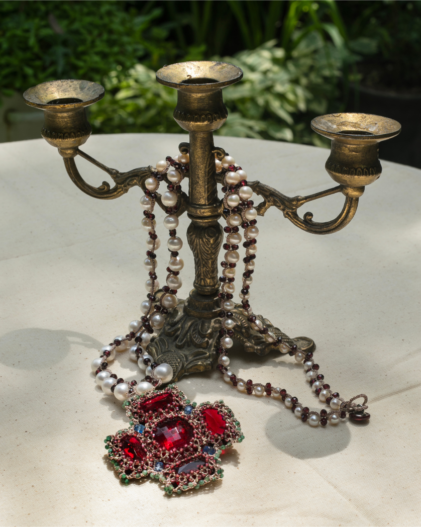 Red silk Anya pendant with intricate beadwork and pearls draped over an ornate brass candlestick holder.