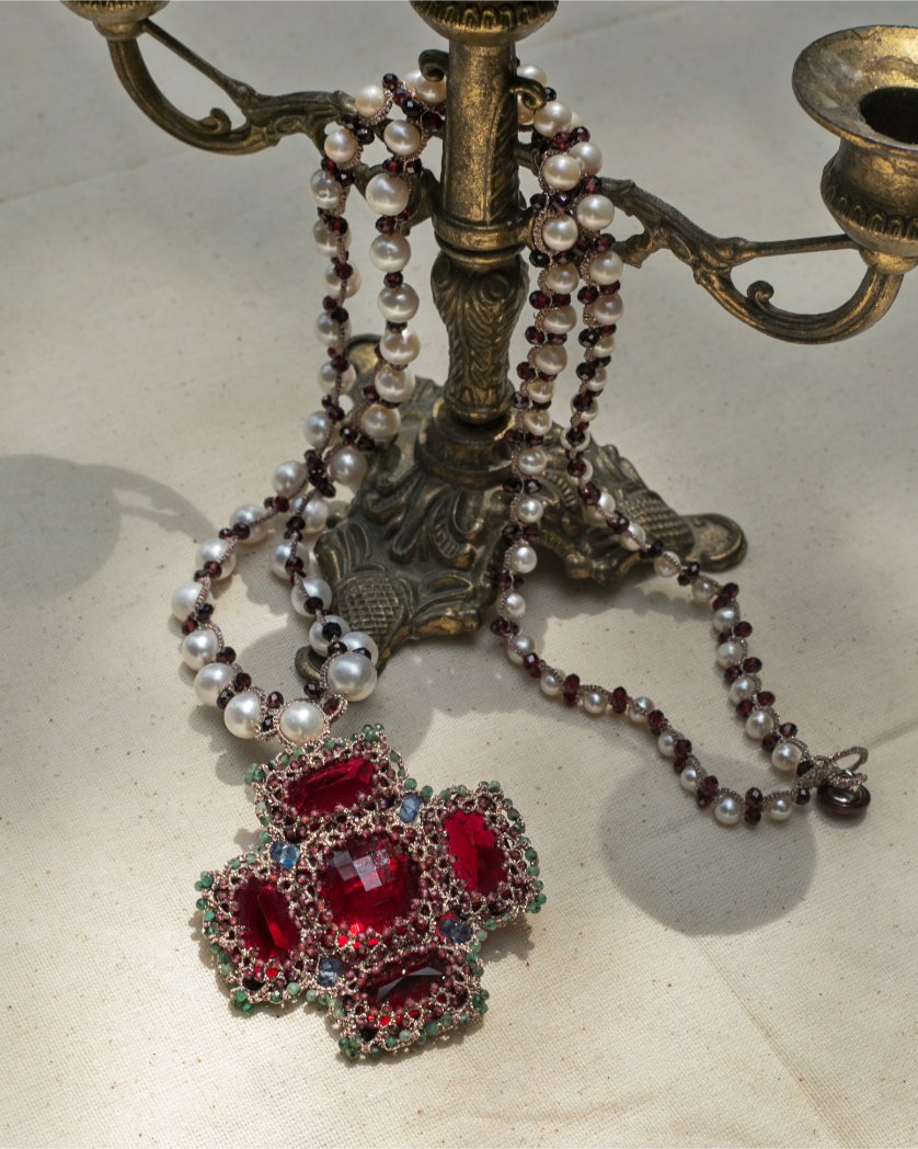 Elegant red silk pendant with intricate detailing, adorned with pearls and gemstones on a vintage brass candlestick.