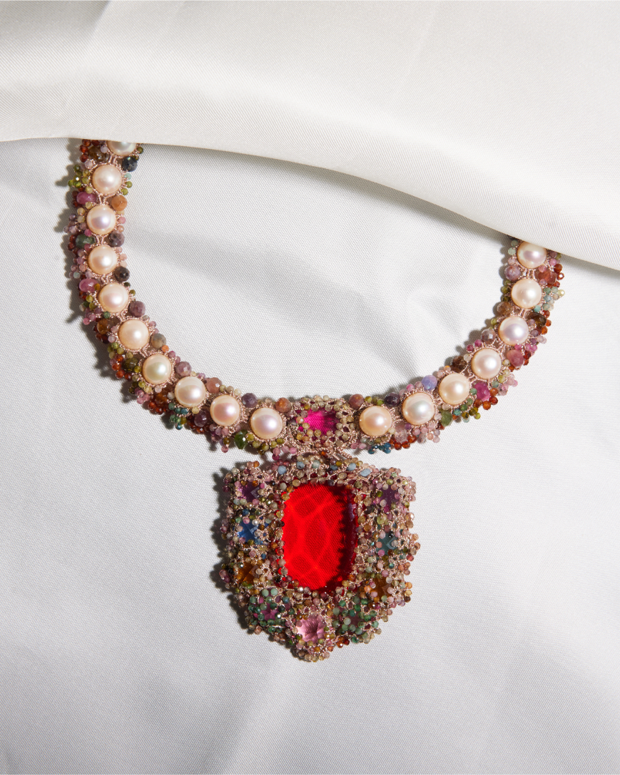CARMEN NECKLACE with pearls, multicolored gemstones, and red center on white silk background.