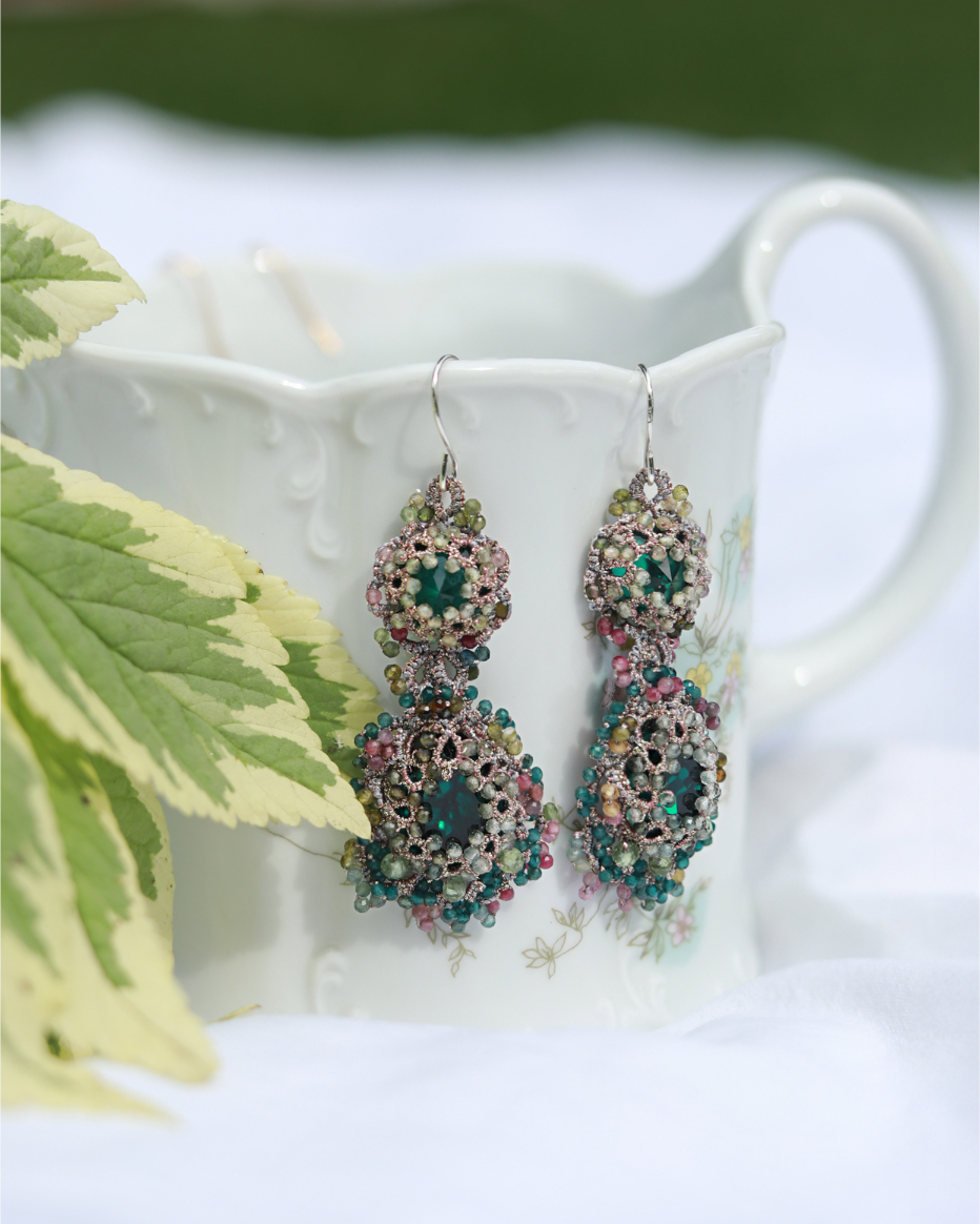 Green silk earrings with intricate beaded design displayed against a floral mug backdrop.