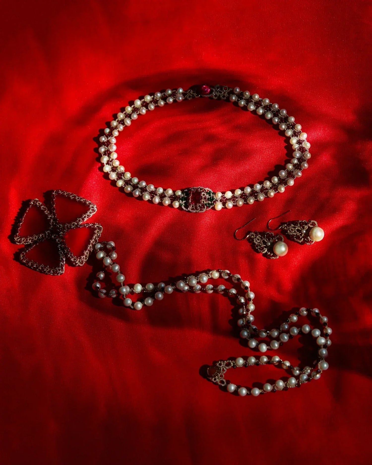 Red silk backdrop with freshwater pearl, garnet pendant details; garnet and pearl accentuated necklace and earrings.