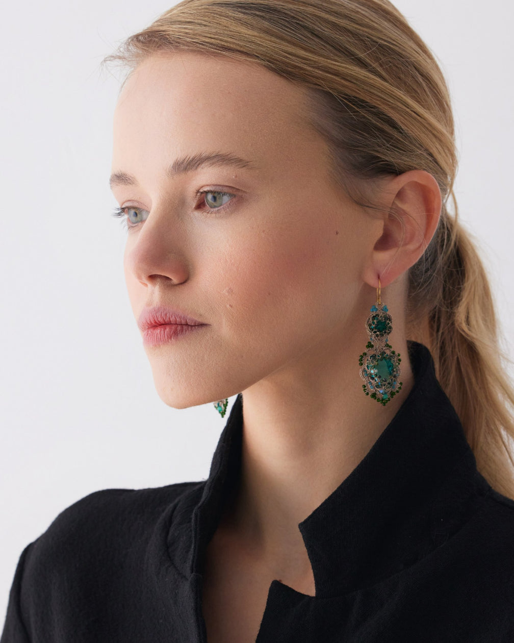 Green INESSE earrings with intricate design, side view, worn by model in black outfit, showcasing detailed craftsmanship.