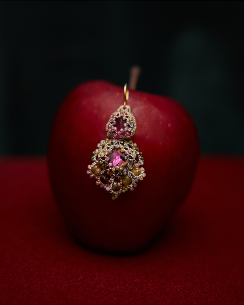 Intricate rose silk Kimberly earrings with delicate beadwork against a red apple background.