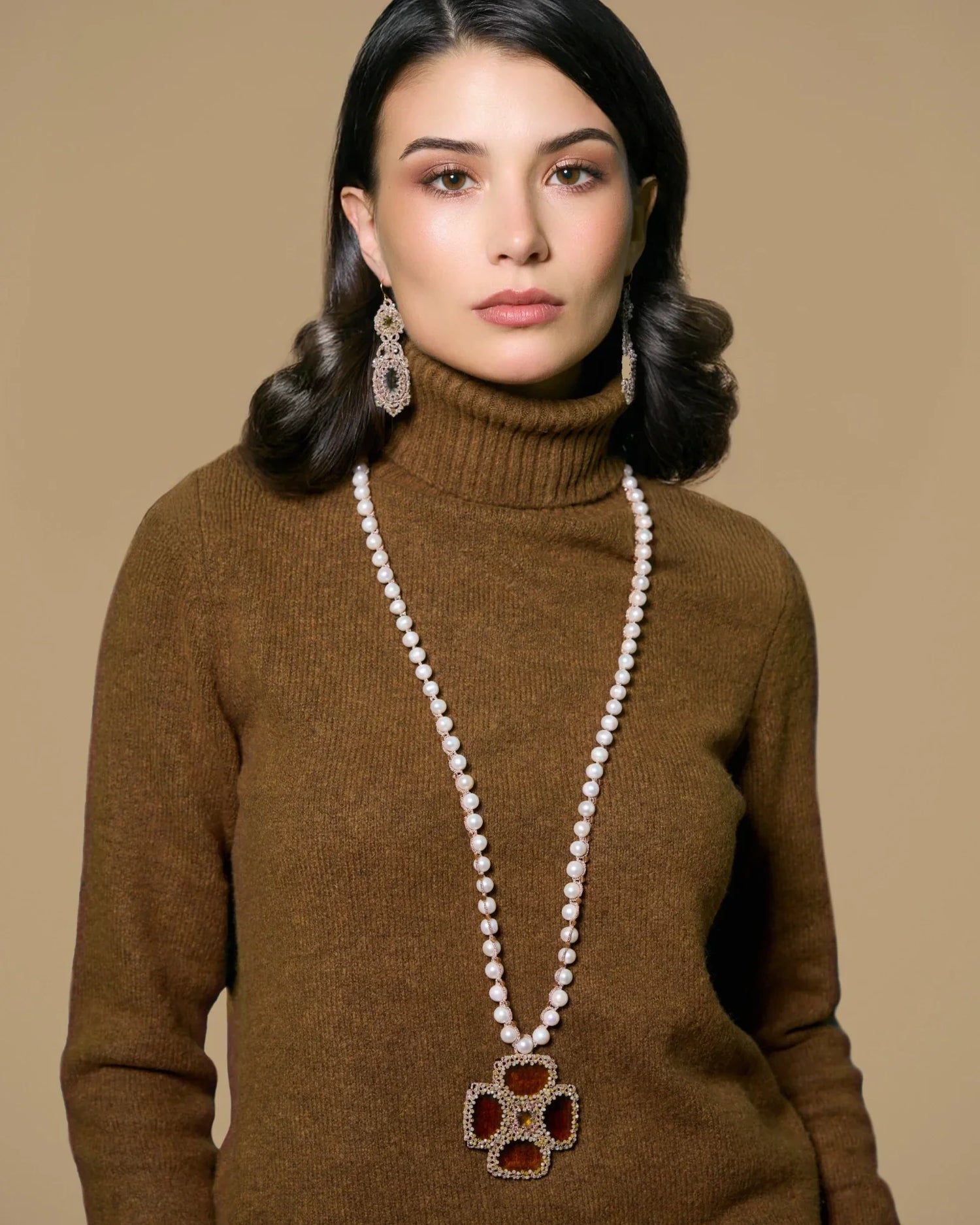 Gold MALTA PENDANT with silk, crystal accent, freshwater pearls, detailed design against brown fabric background.