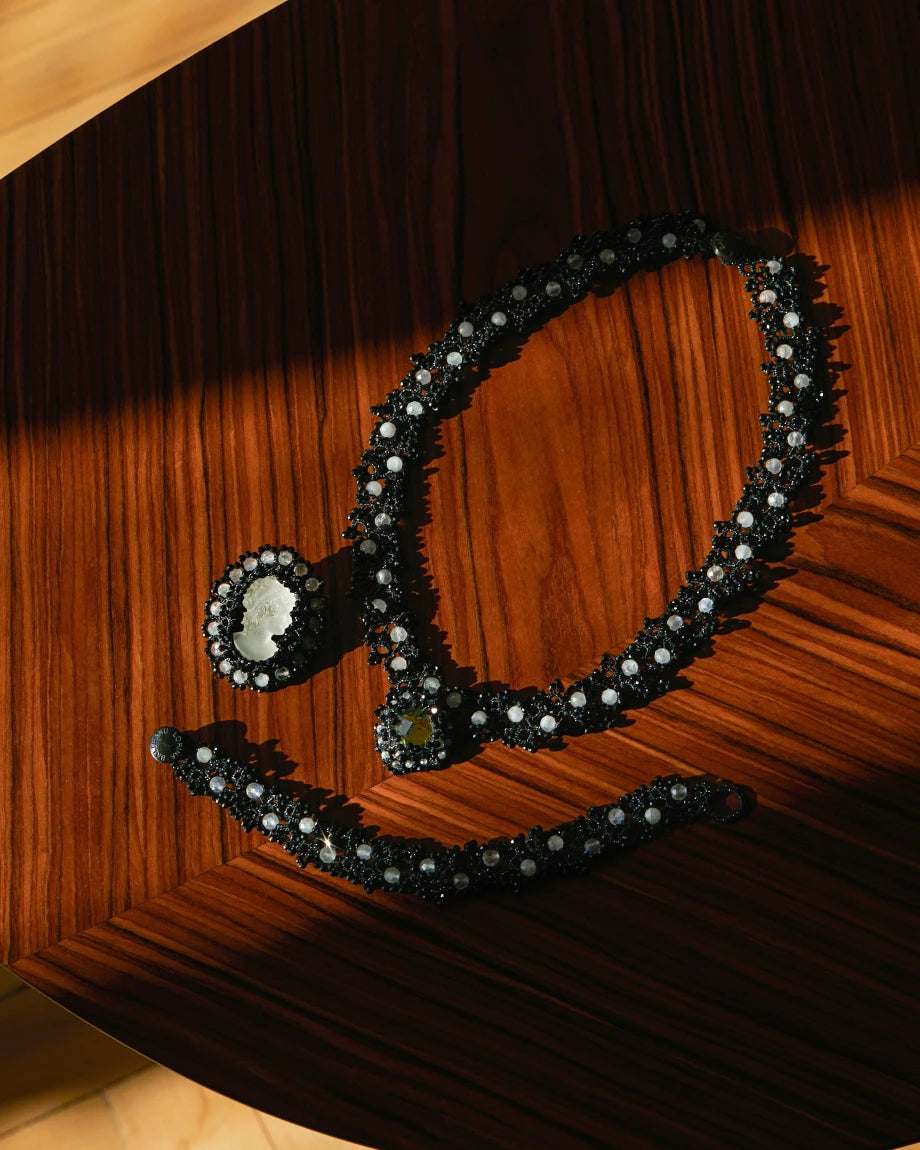 Black silk and silver Margueritte brooch detail with glass accents on wooden surface.