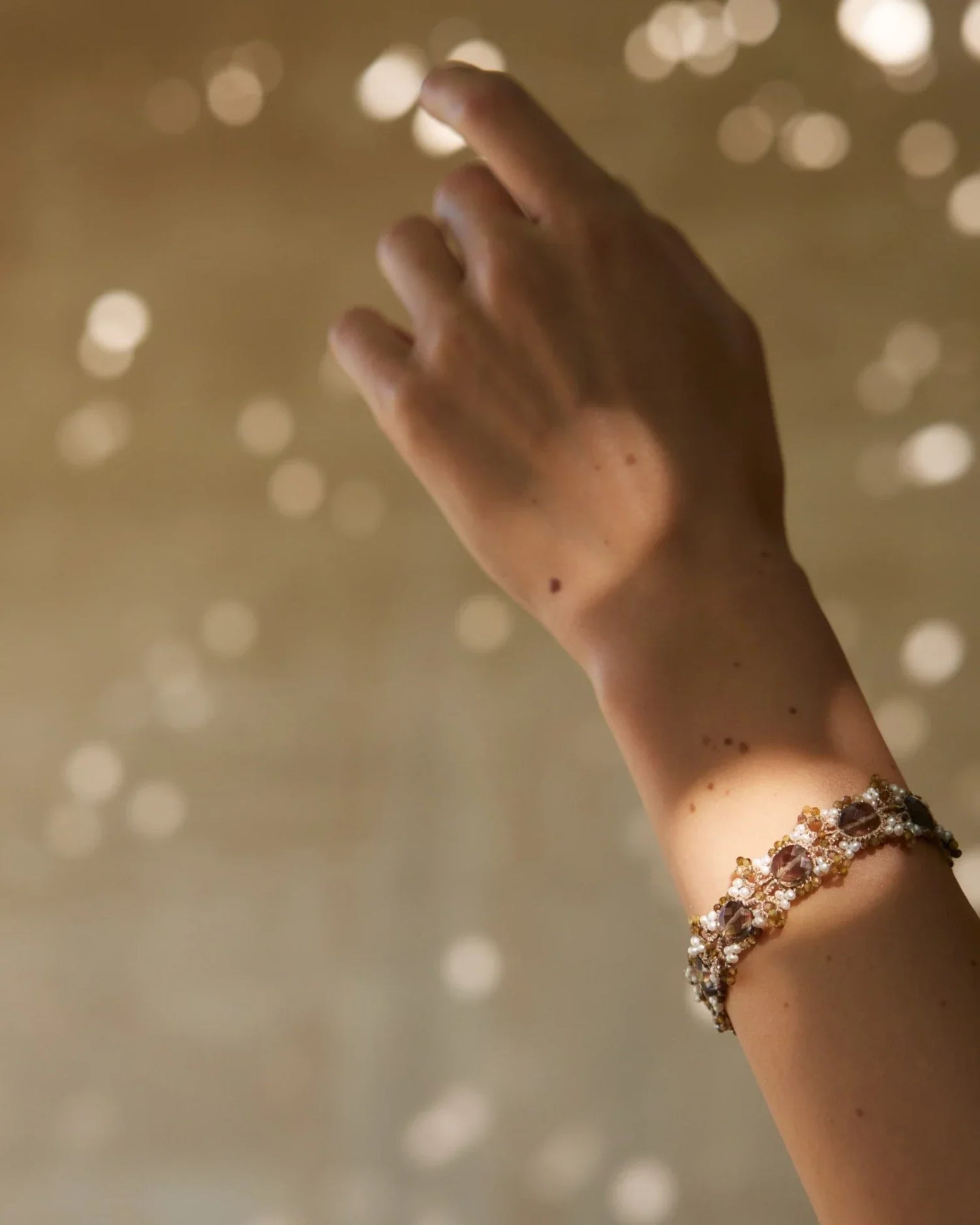 Gold silk bracelet with freshwater pearls and garnet detail, showcasing intricate texture and luminous components.