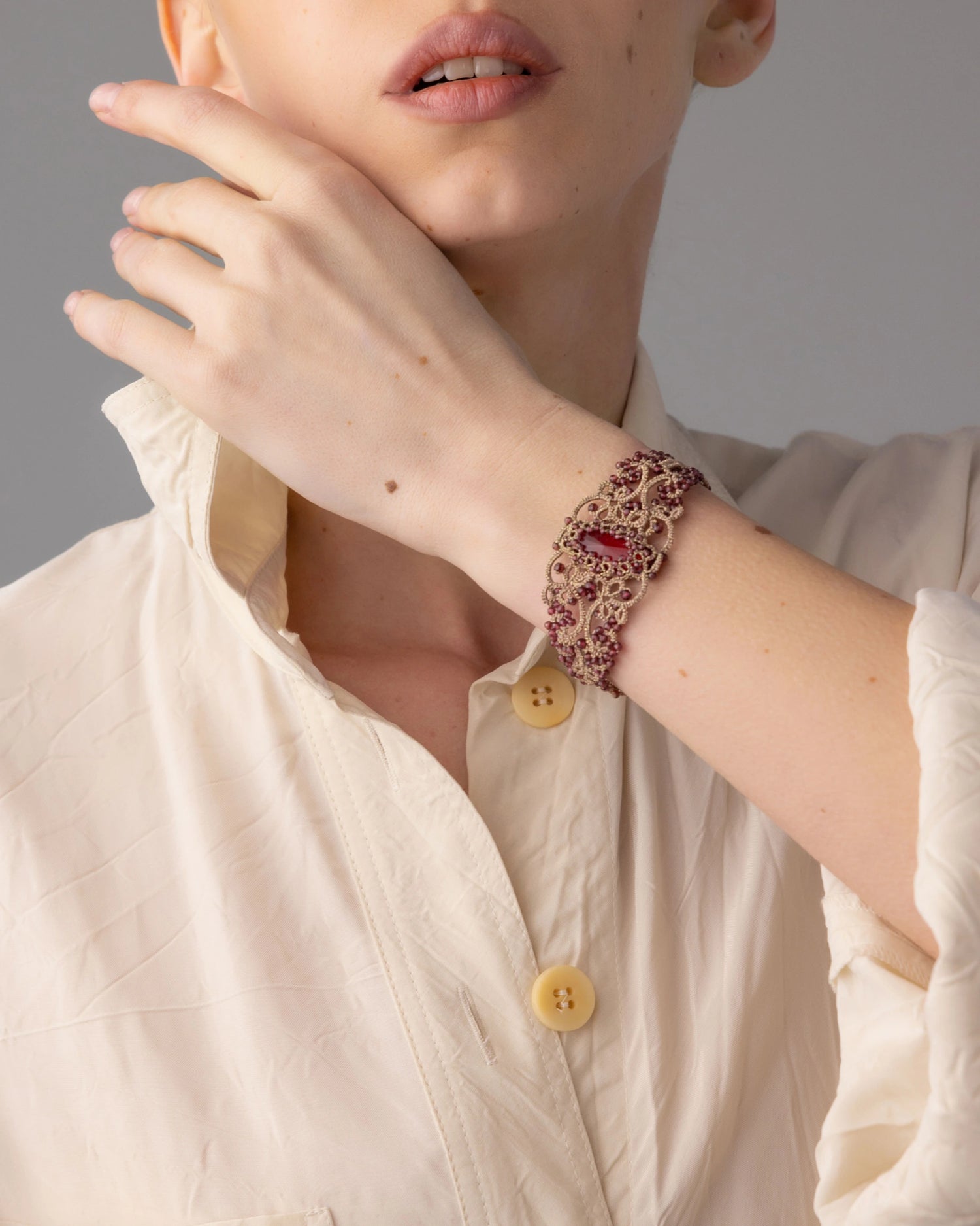 Red silk bracelet with pearls, crystals, garnets, intricate textures, worn on wrist.