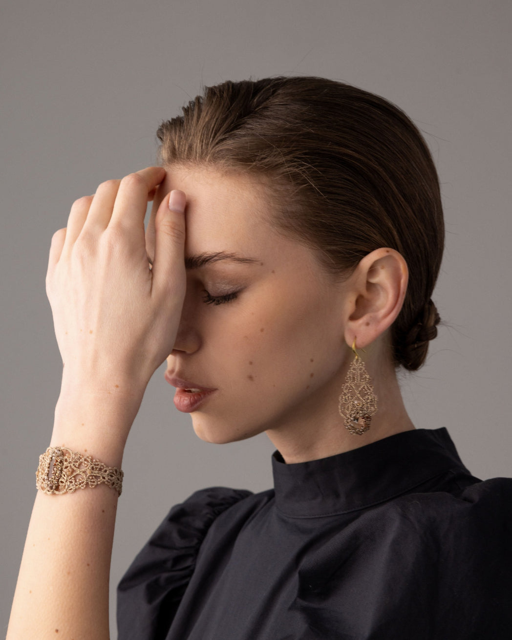 Gold silk earrings with intricate crystal details, worn by model in black attire, showcasing delicate craftsmanship.