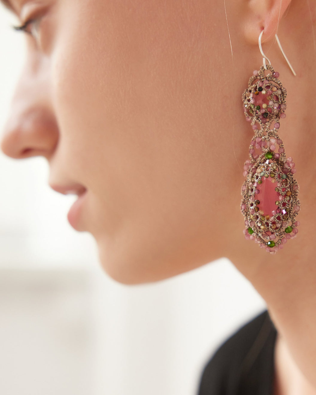 Rose silk earrings with silver hooks, adorned with pink crystals and green tourmaline, detailed texture visible.