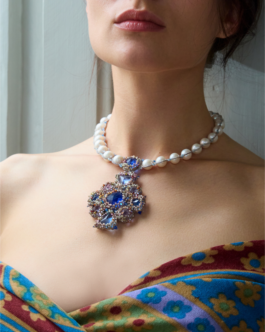 Pearl necklace with a blue gemstone pendant, worn over a colorful floral-patterned silk garment.