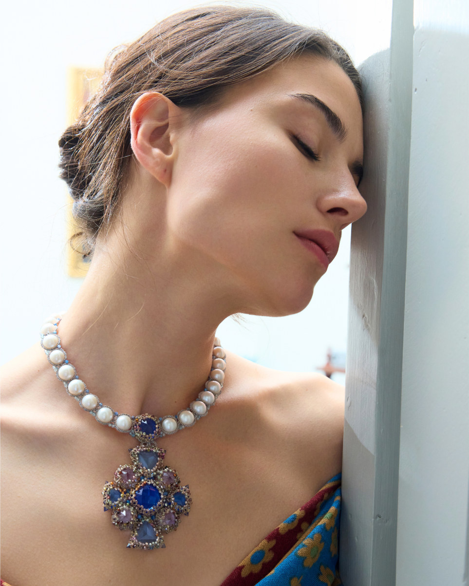 Elegant necklace with purple and blue gemstones on a pearl strand worn by a woman with closed eyes.