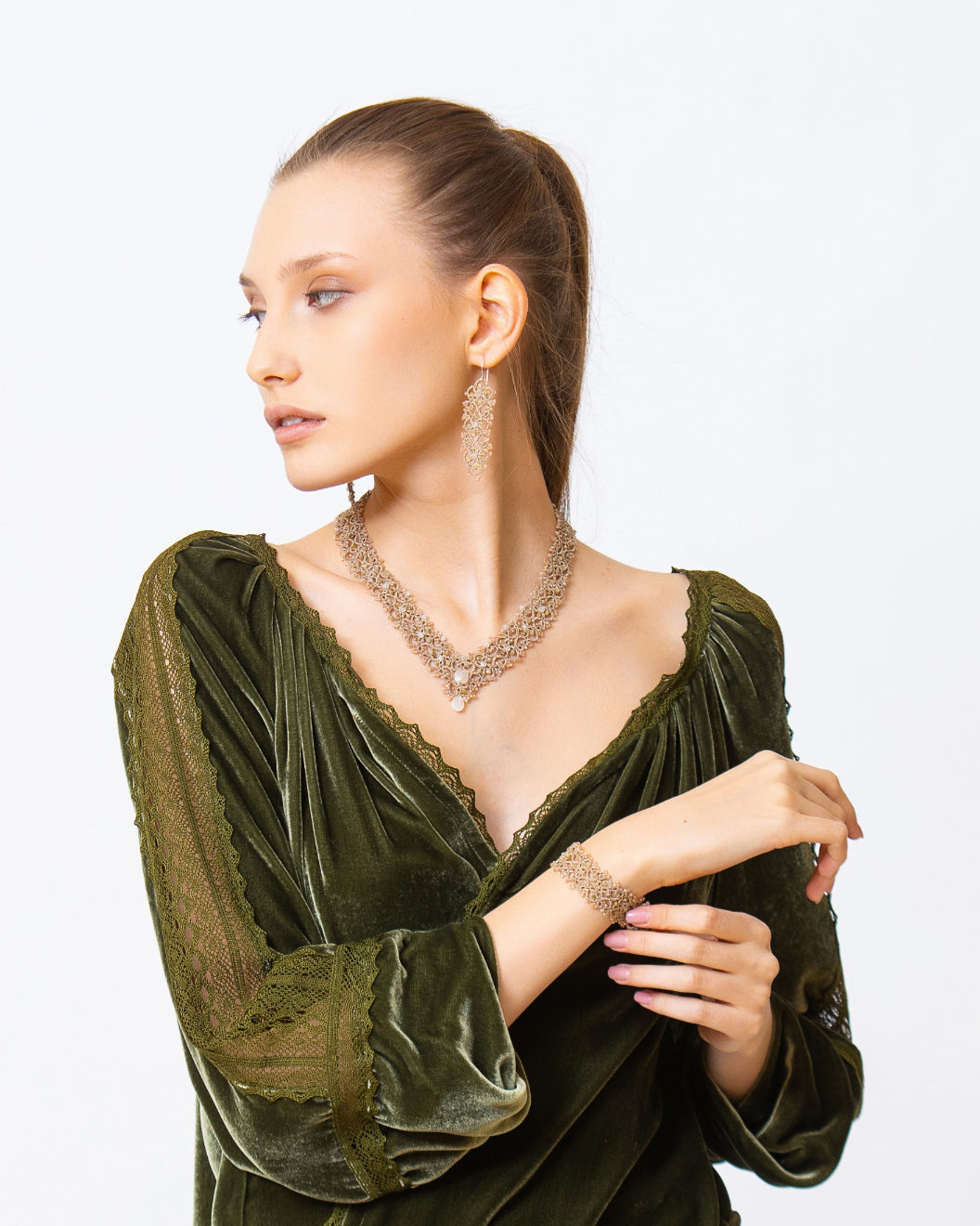 Gold Vintaj bracelet on wrist, intricate chain design, paired with matching necklace and earrings, green velvet top.