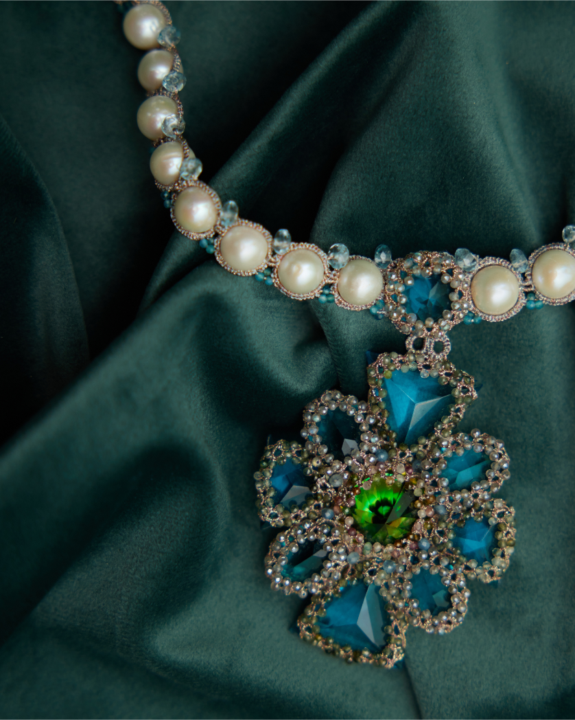 Colier Tiffany cu perle de apă dulce, cristale albastre și detalii de mătase pe fundal elegant.