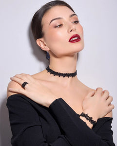 Black silk bracelet detail with pearl accents, worn with matching ring and choker on a woman in a black outfit.