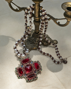 Elegant red silk pendant with intricate detailing, adorned with pearls and gemstones on a vintage brass candlestick.