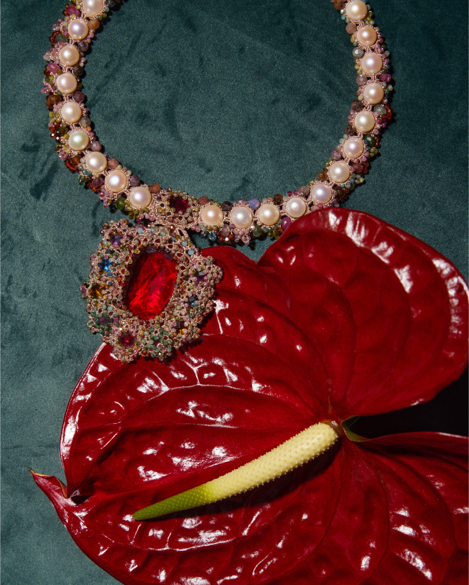 Luxurious pearl-studded necklace on green silk, featuring colorful gemstones and a vibrant red centerpiece.