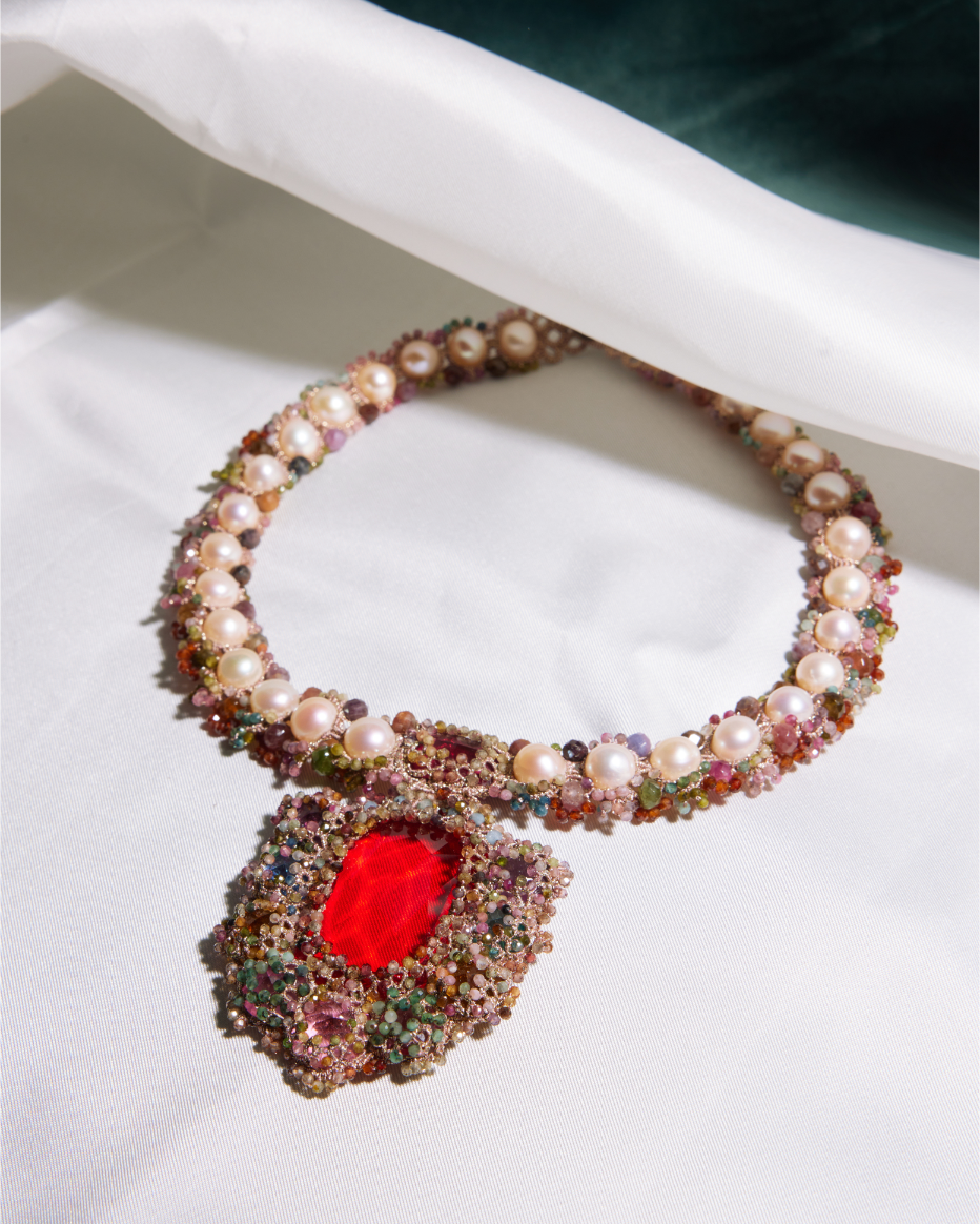 Silk necklace with pearls and multicolored beads, featuring a large red central stone on a white fabric background.