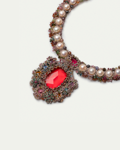 Necklace with red gemstone, pearls, and colorful beads on silk material background.
