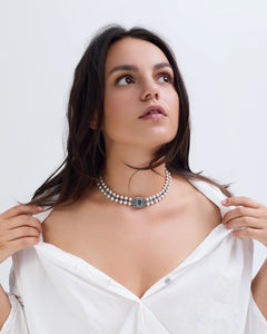 Blue CLEO Choker with pearl strands and ornate blue gemstone clasp in side view worn with white shirt.