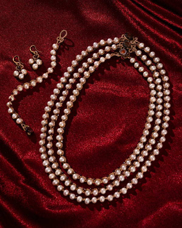 Elegant multi-layered pearl bracelet with matching earrings on rich red fabric backdrop.