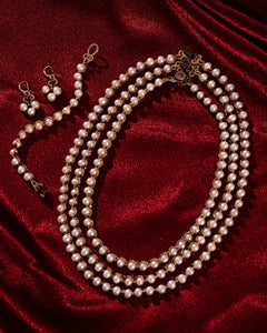 Elegant multi-layered pearl bracelet with matching earrings on rich red fabric backdrop.