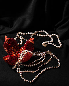 Pearl and garnet necklace with silk thread draped over red pomegranate, highlighting texture and material contrast.