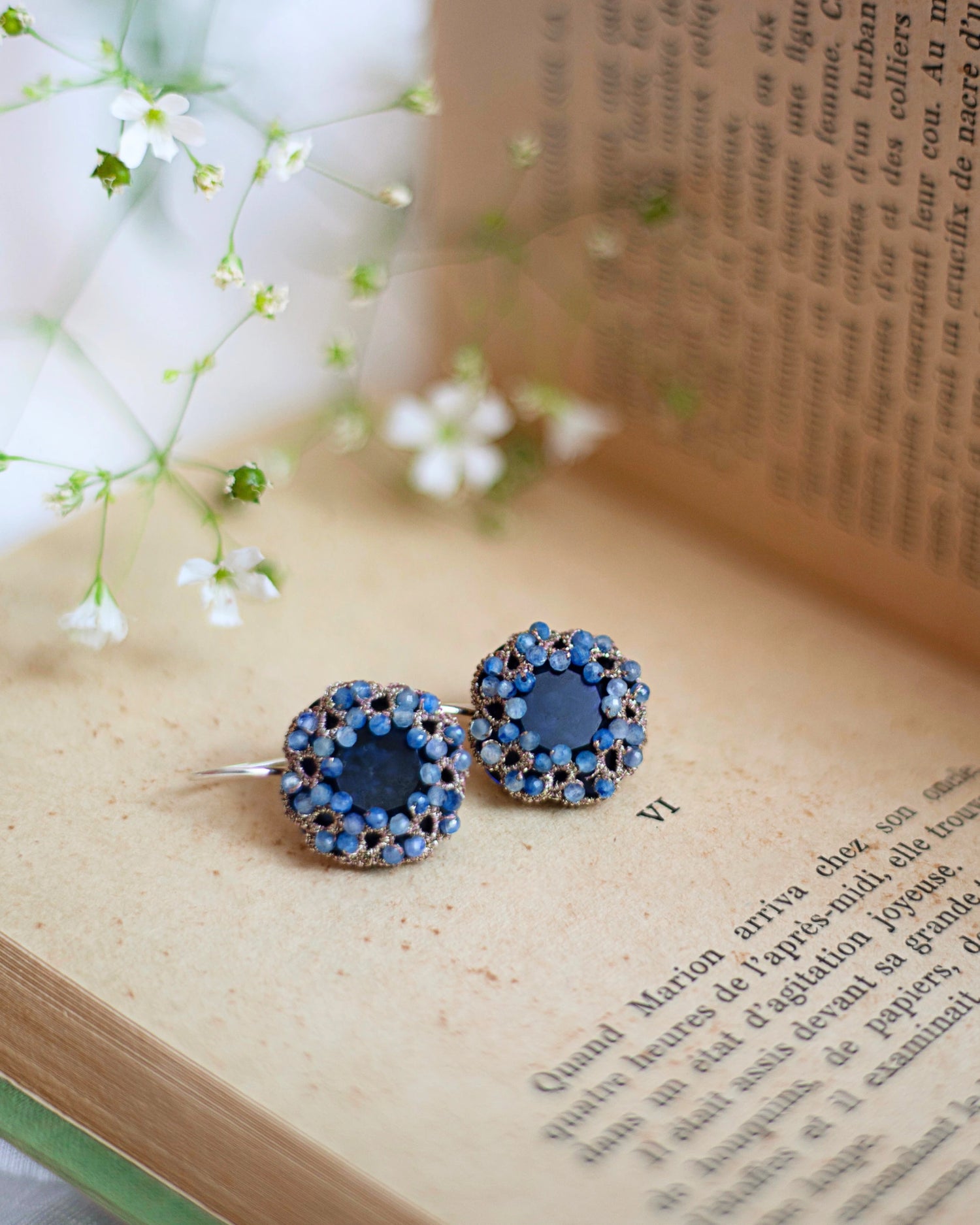Blue silk, silver, crystal, and kyanite earrings with intricate detailing on an open book background.