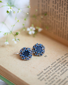Blue silk, silver, crystal, and kyanite earrings with intricate detailing on an open book background.
