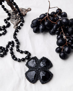 DITA Pendant with black vintage glass, spinel gemstones, silk and pearl detailing, on white background.