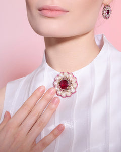 Rose ECATERINA earrings with pearls and red gemstone, gold detailing, seen on model wearing white fabric.