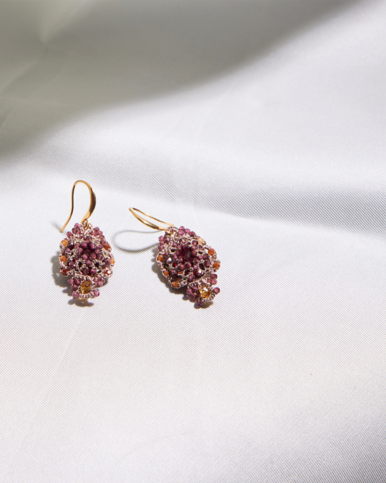 Pink beaded silk earrings with gold accents on smooth white fabric background