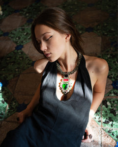 Elegant necklace with silk, pearls, crystals, green sapphire, and red garnet accents on a dark textured fabric.