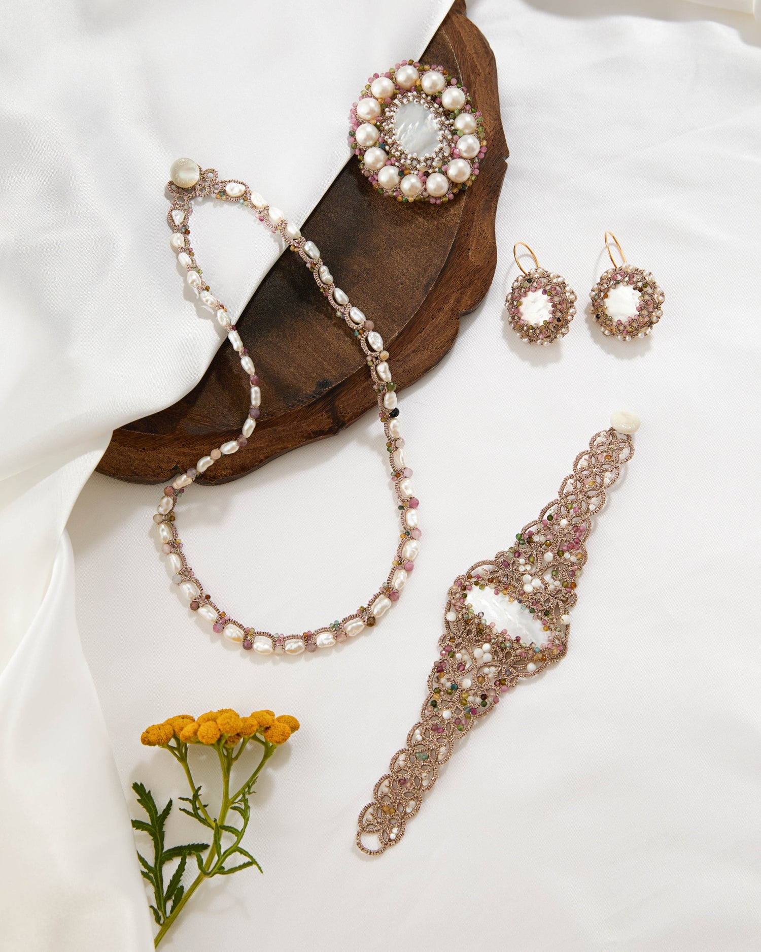 Silk bracelet with freshwater pearls and tourmaline in white, intricate lace-like detailing, displayed on fabric.