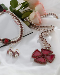 Red silk and freshwater pearl pendant with garnet details on delicate fabric background.