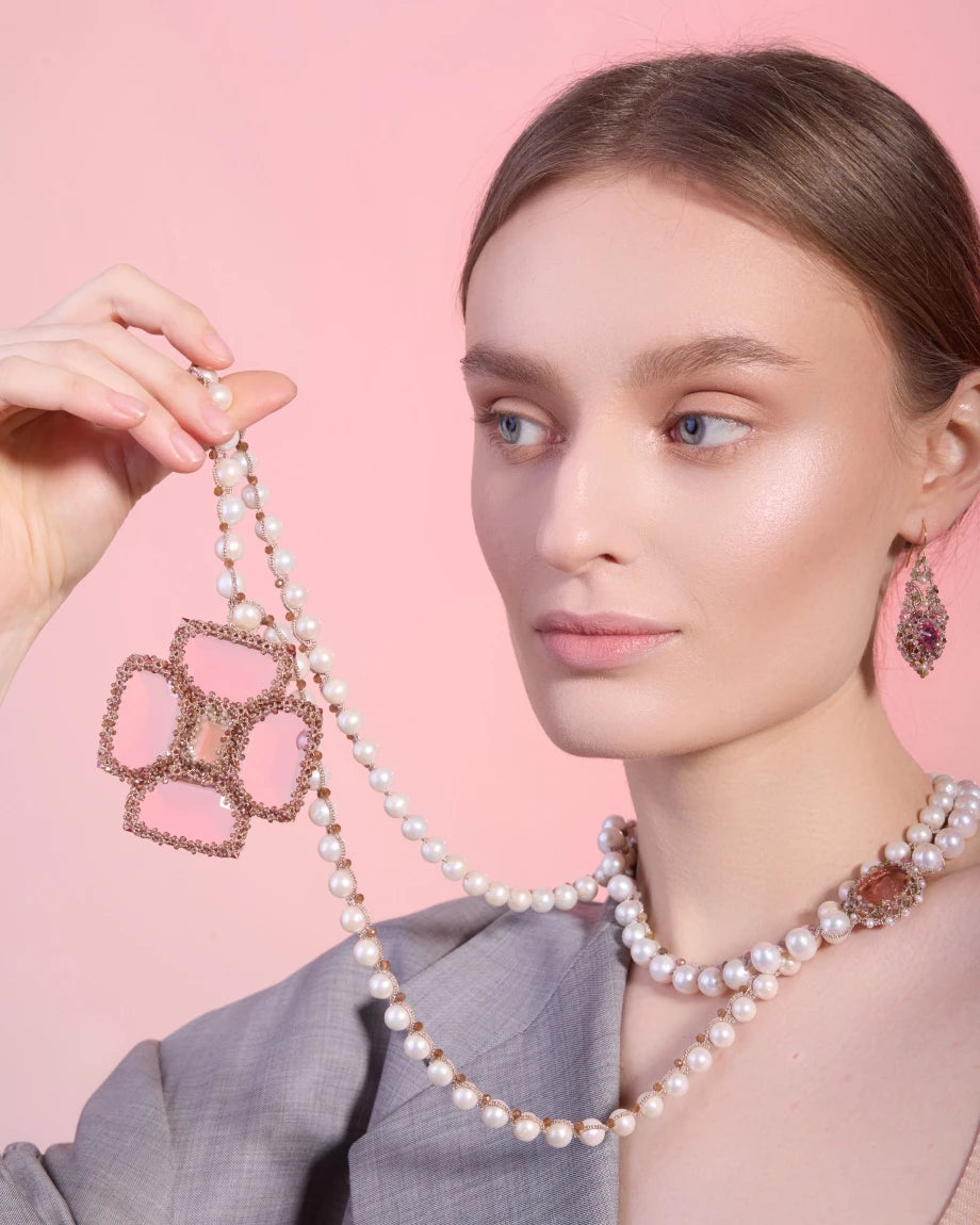 Silk necklace with freshwater pearls and rose tourmaline pendant on woman's neck against pink background.