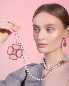 Silk necklace with freshwater pearls and rose tourmaline pendant on woman's neck against pink background.