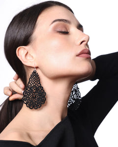 Black lace-like silk earring with intricate pattern, silver hook, worn by model against a white background.