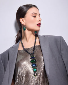 Black freshwater pearl pendant with layered green and blue glass details, worn with a metallic outfit.