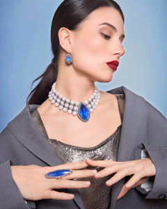 Blue Hepburn necklace with pearl strands, blue gemstone center, worn with matching earrings and ring, silver top.