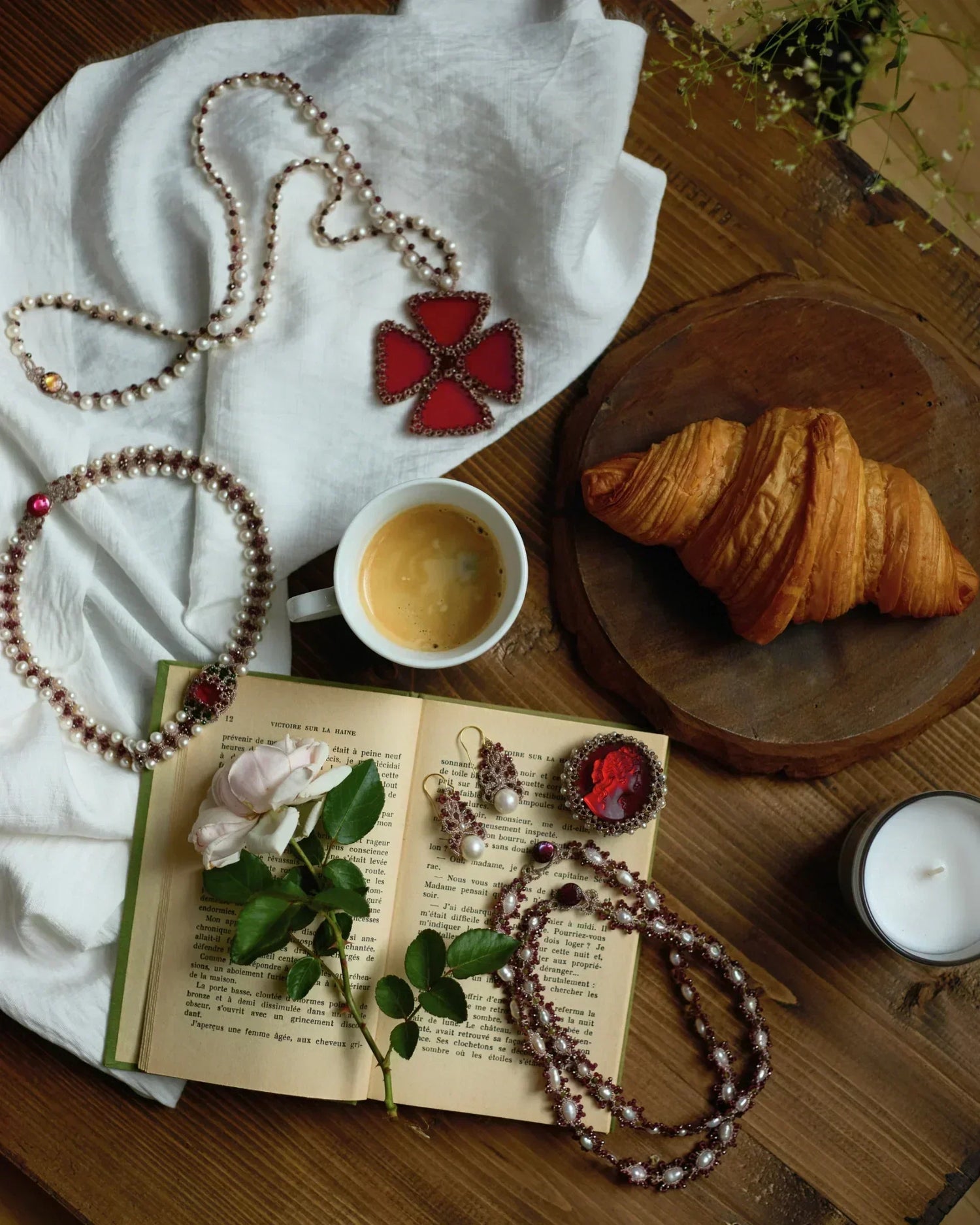 Red silk and pearl choker detail with freshwater pearls and garnet, displayed on a wooden table with an open book.