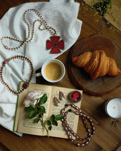 Red silk and pearl choker detail with freshwater pearls and garnet, displayed on a wooden table with an open book.