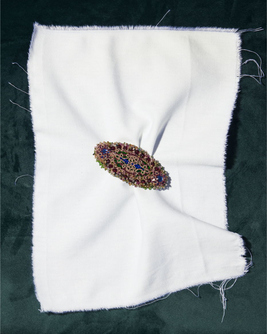 JENNA BROOCH with multicolor gemstones, silk, silver details on white fabric background.