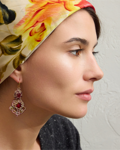 Red gemstone drop earring in ornate gold setting, side view on a model with floral headscarf.