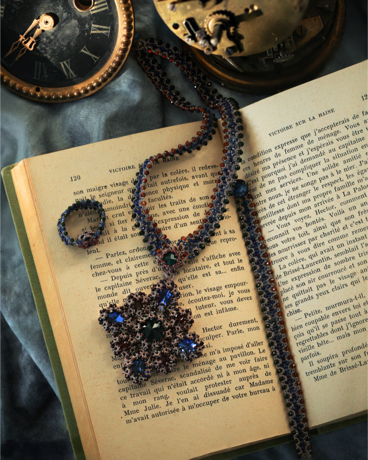 Multicolor LINDA RING in silk, crystal, and garnet on vintage book page with intricate detailing and rich texture.