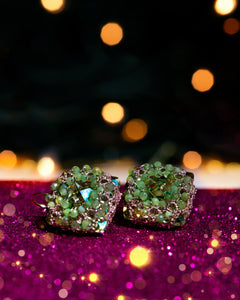 Green LORELEI EARRINGS with silk, gold, silver, and crystal details on glittery pink background.