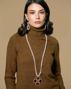 Gold MALTA PENDANT with silk, crystal accent, freshwater pearls, detailed design against brown fabric background.