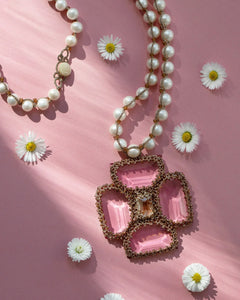 Rose Malta pendant with pearl necklace, featuring intricate beading and ornate crystal design, on floral pink background.