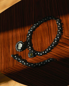 Black silk and silver Margueritte brooch detail with glass accents on wooden surface.